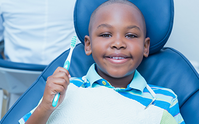 A young boy holding a toothbrush in the dentist chair