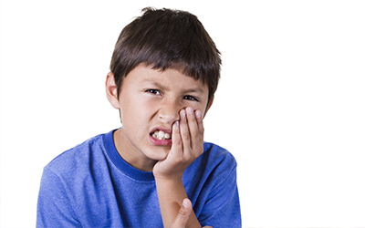 A young boy holding the side of his mouth in pain