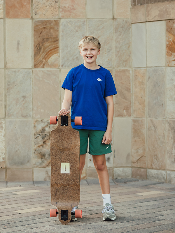 A young boy staing tall and smiling with his skateboard