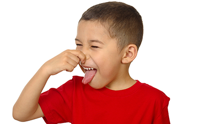 A young boy plugging his nose and sticking his tongue out. 