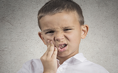 A young boy holding the side of his mouth in pain