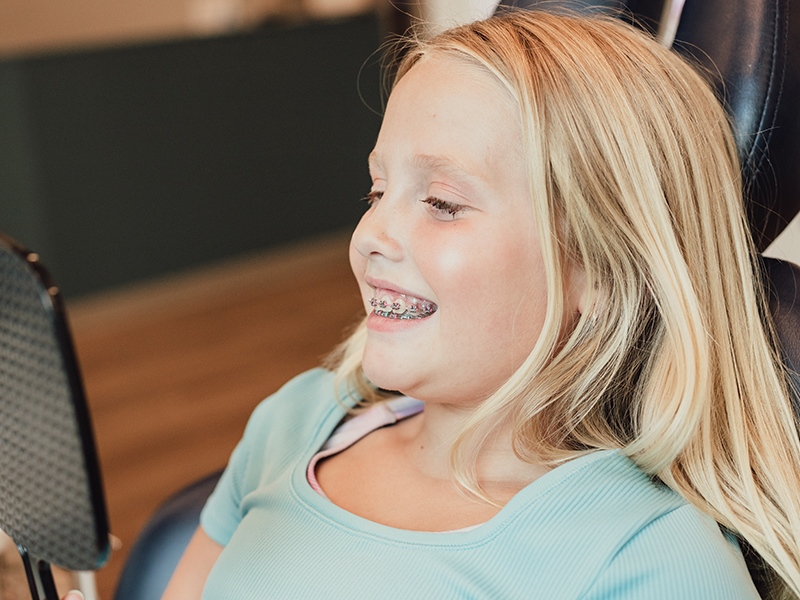 A young child in dental chair adjusting her dental braces in Firestone, CO