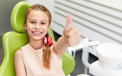 Child in dental chair with thumbs up