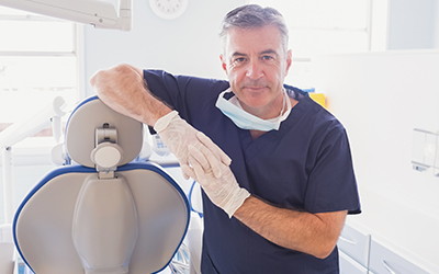 Smiling male dentist leaning against a dental chair