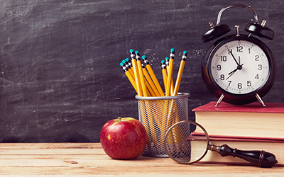 An apple, pencils, clock and books in a school setting