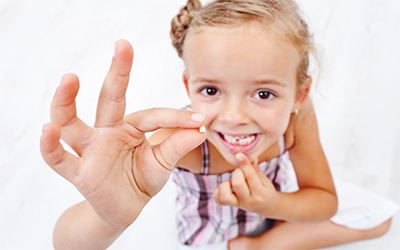A young girl holding up a missing tooth in her hand